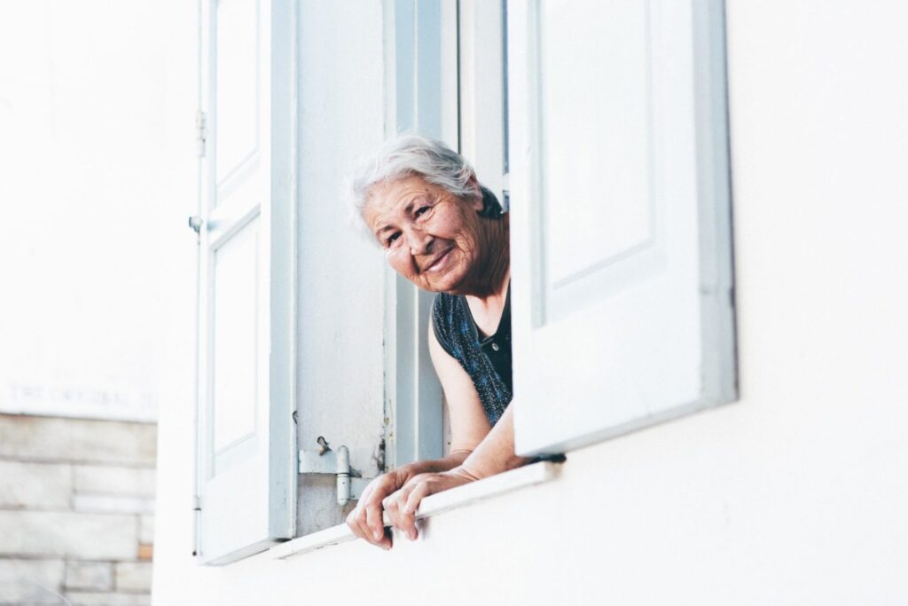 Alternatives aux EHPAD : femme âgée souriante et heureuse qui admire l'environnement à partir de la fenêtre de sa chambre.