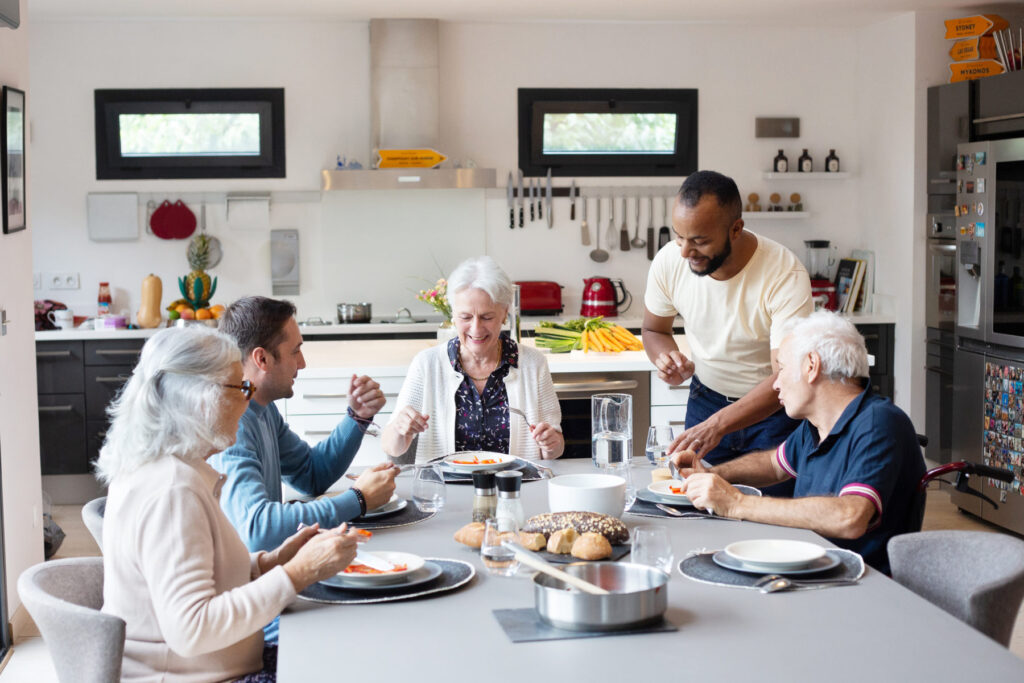 Quatre colocataires prennent leur repas pendant que l'assistant de vie les accompagnes