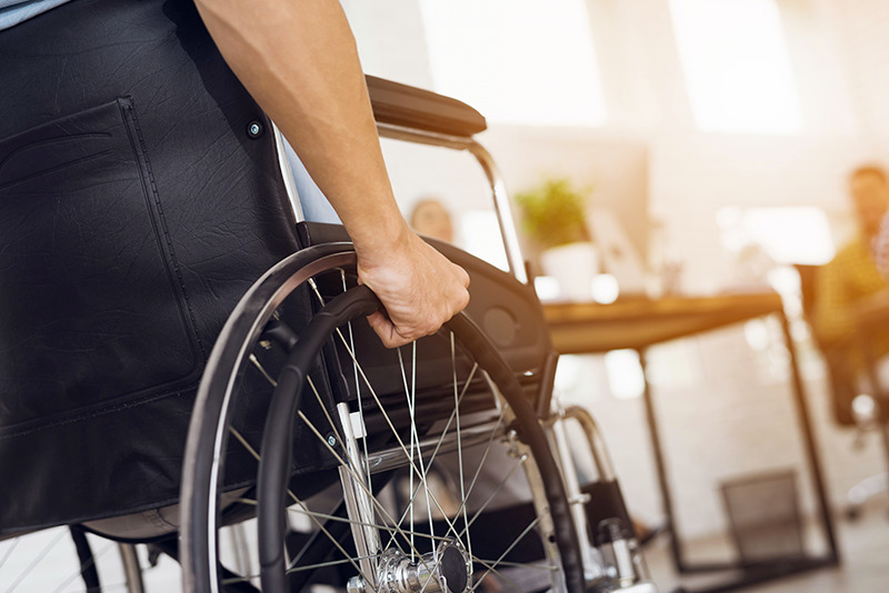 Allocation aux adultes handicapés : la main d'un homme handicapé sur la roue de sa chaise roulante.