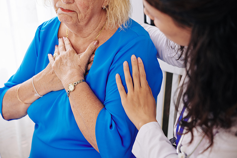 Femme senior souffrant d’arythmie cardiaque, se tenant la poitrine, accompagnée par une médecin qui la soutient et l’épaule pendant l’examen médical.