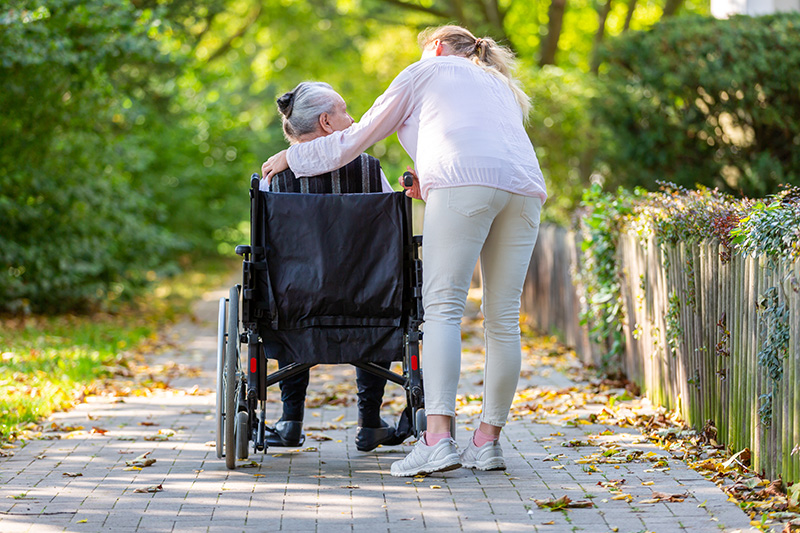 Congé proche aidant : Une femme de 45 ans, qui accompagne sa mère, sur une chaise roulante, dans un joli parc vert.