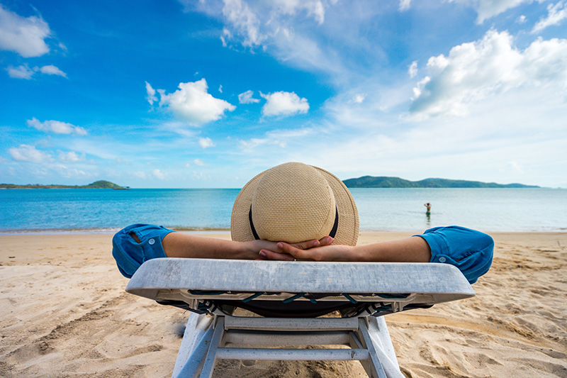 Séjour de répit : une femme en chapeau de paille, allongée sur une chaise longue, à la plage sous un beau ciel.