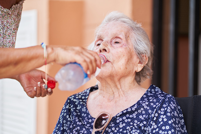 Déshydratation personne âgée : une femme âgée, déshydratée, qui boit de l'eau grâce à l'aide d'une autre personne.