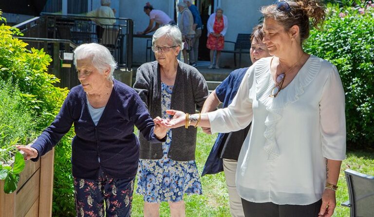 Des personnes âgées, de différents niveaux e GIR accompagnées par des assistantes de vie dans le jardin d'une colocation seniors.