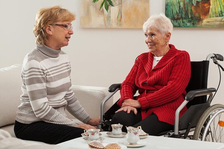 Dans leur habitat inclusif, deux femmes âgées, dont l’une en fauteuil roulant, discutent ensemble autour d’un café.