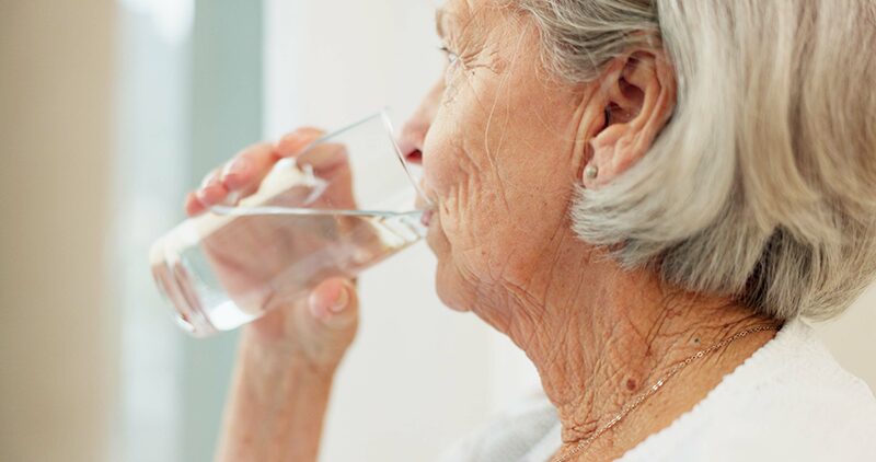 Femme âgée buvant un verre d’eau pour prévenir la déshydratation et limiter les risques d’hypernatrémie chez les seniors.