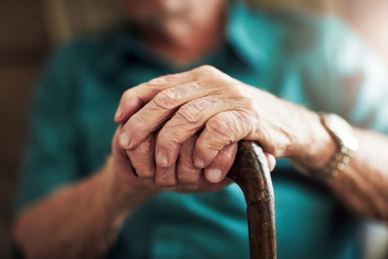 Loi grand âge : mains d’une personne âgée posées sur une canne, illustrant le besoin de soutien, de dignité et d’accompagnement dans le grand âge.