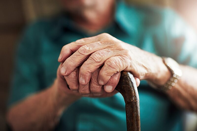 Loi grand âge : mains d’une personne âgée posées sur une canne, illustrant le besoin de soutien, de dignité et d’accompagnement dans le grand âge.