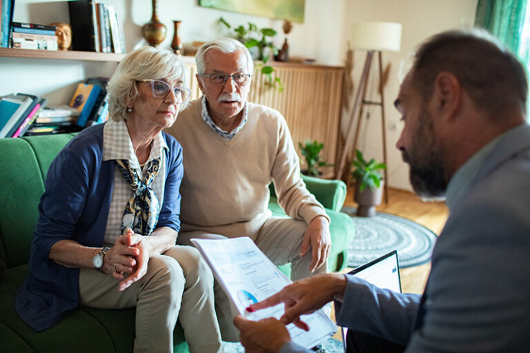 Un couple de seniors assis sur un canapé, discutent avec un avocat des lois clés protégeant les personnes âgées.