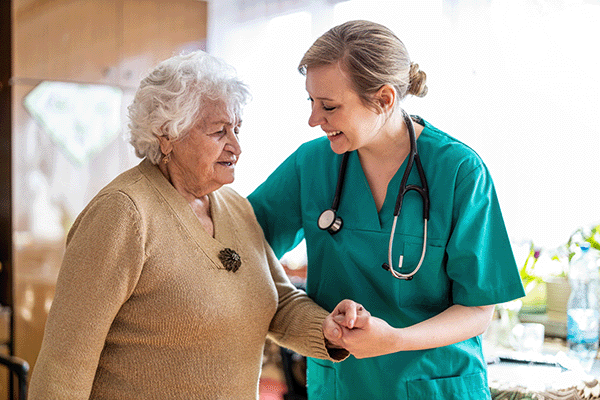 Une médecin coordonnateur, jeune et souriante, qui tient la main d'une femme âgée après la consultation.