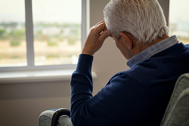 Une personne âgée atteinte de TDAH qui est assis main sur le front devant la fenêtre de sa chambre.