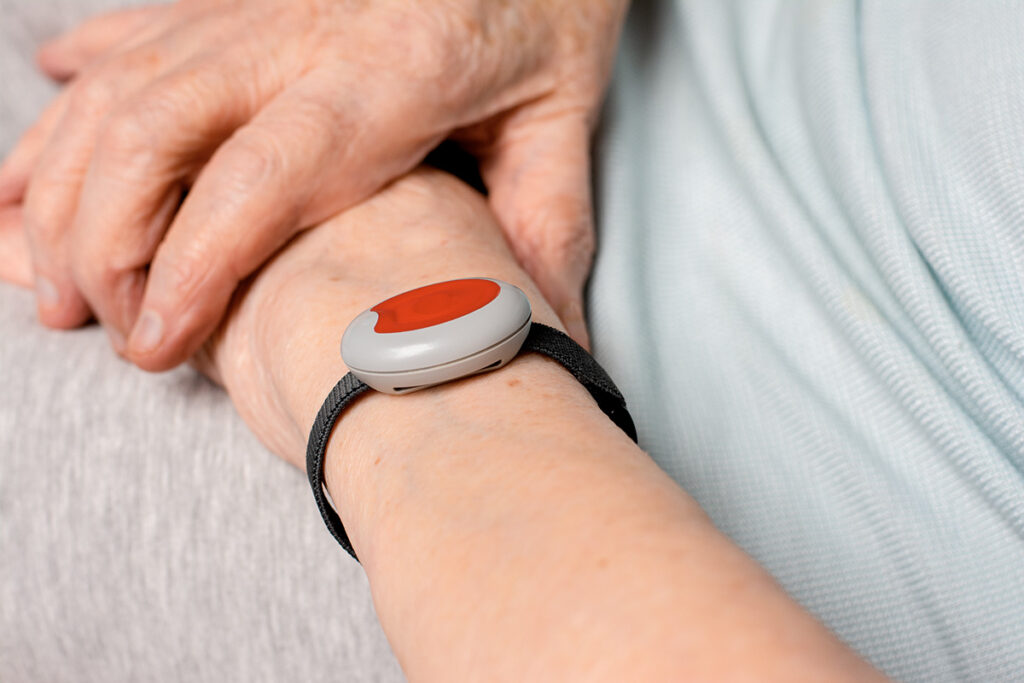 Poignet d’une personne âgée portant un dispositif de téléassistance gratuite, avec un bouton d’alerte rouge.Poignet d’une personne âgée portant un dispositif de téléassistance gratuite, avec un bouton d’alerte rouge.