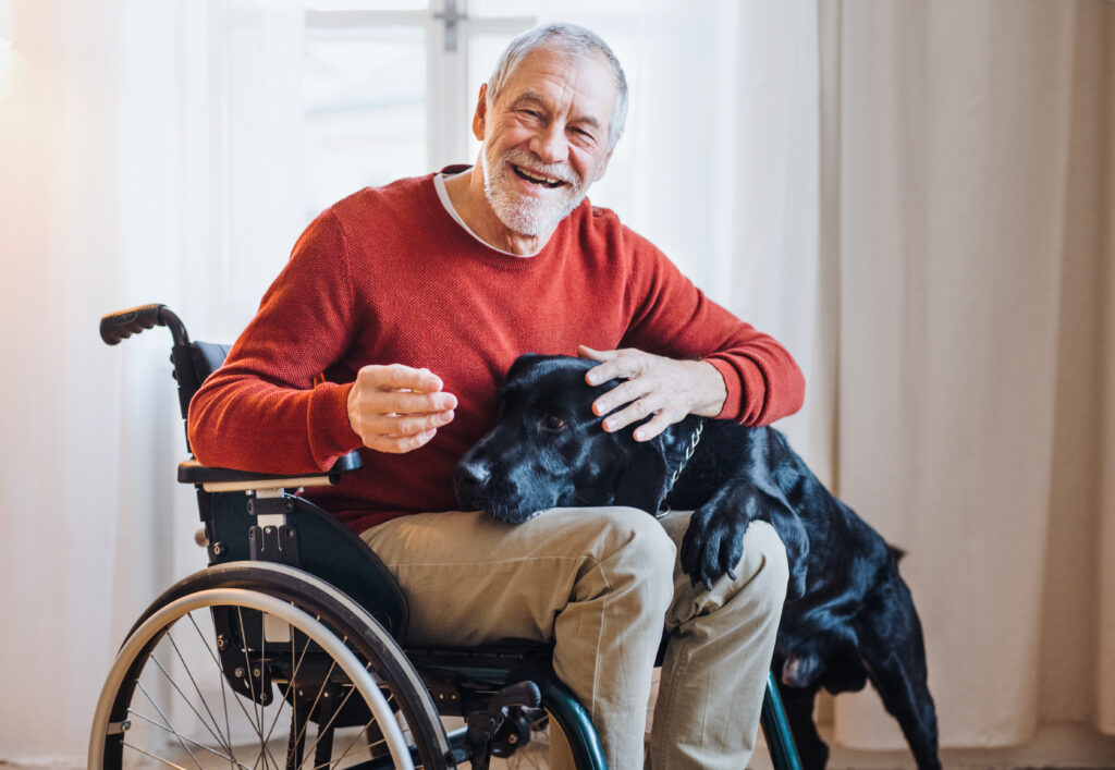 Une personne âgée en fauteuil roulant accompagné par son chien dans sa maison