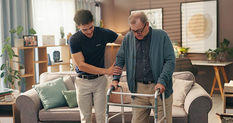 Aidant naturel, jeune homme accompagnant son proche qui se déplace avec un déambulateur.