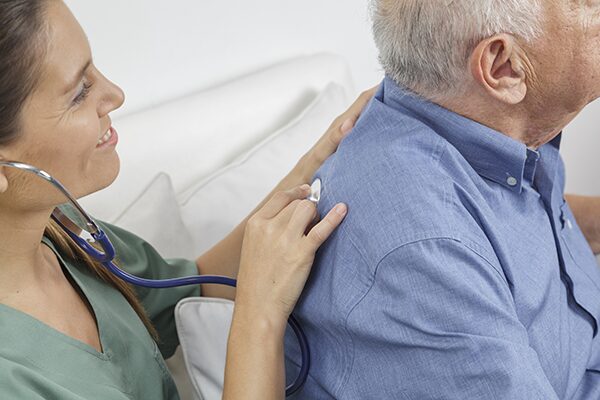 Un homme âgé se fait ausculter le dos pour prévenir d'une éventuelle embolie pulmonaire par une médecin.