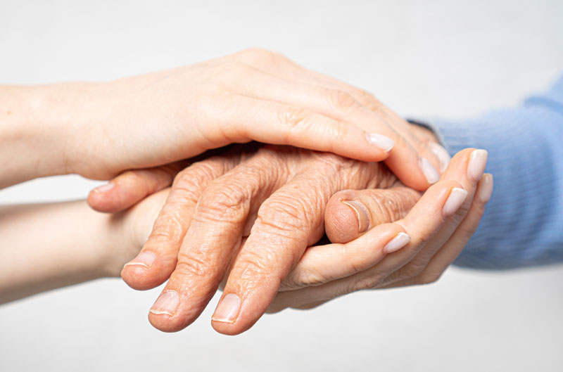 Une dame tient entre ses mains la main d'une personne âgée