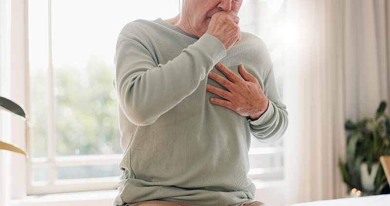 Une personne âgée entre train de tousser avec une main sur la poitrine à cause d'une infection pulmonaire