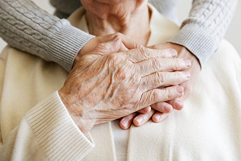 Les mains d’une fille posées sur celles de sa mère âgée, un geste de soutien et de réassurance illustrant la sérénité apportée par le mandat de protection future.