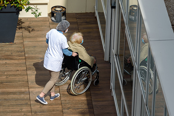 Une infirmière pousse le fauteuil d'une personne âgée pour entrer dans l'EHPAD